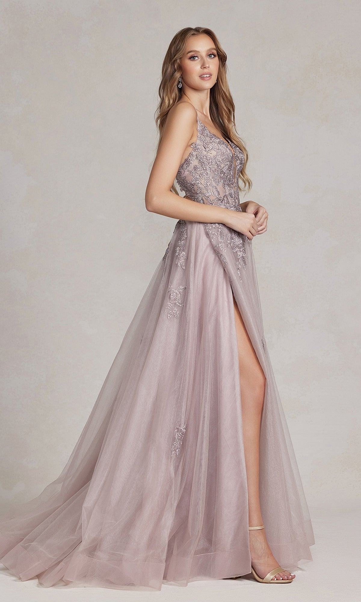 A woman stands against a neutral background in the Open-Back Long Prom Ball Gown with Beads—a sleeveless, floor-length lavender A-line dress featuring beaded lace appliques and a high slit.